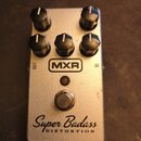Stříbrný efekt pedál s pěti černými ovládacími knoflíky. Na přední straně je umístěno logo MXR, nápis Super Badass a pod ním slovo DISTORTION. V horn…