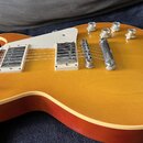 Elektrická kytara s žlutým gradientem (sunburst) a bílým pickguardem. Na kytaru jsou instalovány dva humbuckery s kovovými kryty a čtyři ovládací kno…