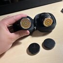 Dva černé cylindrické mikrofony umístěné v černém zipovém pouzdře. Na přední straně mikrofonů jsou vidět zlaté koncentrické kruhy membrán. Před pouzd…