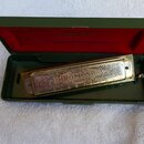 Chromatická harmonika v zeleném originálním pouzdře s červeným vnitřkem. Na krytce nástroje je nápis SUPER CHROMONICA a níže text CHROMATIC HOHNER HA…