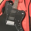 Černá elektrická kytara s černým pickguardem a hnědým hmatníkem. Nástroj má dva humbuckery, chromovaný kobylník a dva oválkové knofíky s nápisy VOLUM…