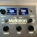 Detail ovládacího panelu stříbrného přístroje s nápisem Mellotron STOCKHOLM - LOS ANGELES. Panel obsahuje dva malé displeje, z nichž levý nese nápisy…