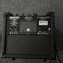 Zadní strana černého kytarového komba s nápisem JOYO Digital Guitar Amplifier Model No.:DC-15. Na zadním panelu jsou vidět vstupy AUX IN a PHONES, vy…