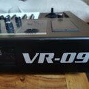Černý klávesový nástroj s bílými klávesami. Na boční straně je velký bílý nápis VR-09 a nad konektorem USB je text USB COMPUTER. Na horním panelu jso…