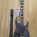 Elektrická kytara s tmavým dřevěným povrchem a šedou hlavou, na které je bílý nápis Ibanez. Kytara má dva humbuckery, prohnutý most a hриф s vkládaný…