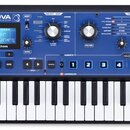 Modrý syntetizátor s klávesnicí a nápisem MININOVA SYNTHESIZER. Na přístroji je vidět displej s textem Vocoder Voc/Tune, logo novation a řada ovládac…
