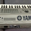Šedý digitální klavír s bílými a černými klávesami. Na boku je viditelné modré logo s nápisem YAMAHA a v dolní části štítek s textem MOTIF 6, SÉRIE N…
