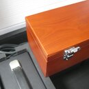 Dřevěný obdélníkový box v hnědém odstínu s kovovým zapínáním. Na pravé straně boxu je viditelné oválné logo s nápisem LLP. Vedle boxu v černé výplni…