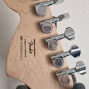 Zadní strana hlavy světlé dřevěné elektrické kytary s šesti chromovanými ladicími mechanismy. Na dřevě je černý nápis „Designed and Backed by Fender…
