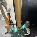 Zadní strana elektrické kytary v kovově zelené barvě s hnedým krčkem z dřeva. Na zadní straně těla je vidět kovový kryt elektroniky s nápisem "L7". P…