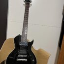 Černá elektrická kytara s dvojstupňovými humbuckery a bílým lemováním těla. Na hlavě je nápis "banez" a logo "Banez". Nástroj vykazuje mírné opotřebe…