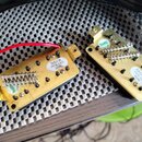 Dva elektrické snímače s kovovými kryty zlaté barvy a černým tělem. Na levém je nápis NECK PICK UPS BHK a na pravém BRIDGE PICK UPS BHK. Oba mají vid…