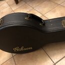 Černý tvrdý kufýr na kytaru s texturovaným povrchem. Na horní části je umístěna zlatá značka Gibson. Kufýr má kovové zapínání a úchyt v mosazném odst…