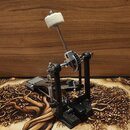 Černý bicí pedál s kovovými mechanismy a řetězovým pohonem. Na beateru je nasazena bílá plišová hlavice. Nástroj nemá žádné viditelné značky ani nápi…