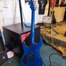 Modrá elektrická kytara s tvarem double-cutaway. Na hlavě je viditelné logo "Ibanez". Zadní strana kytary obsahuje černý kryt elektroniky a černý kry…