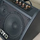Černý kytarový kombo zesilovač s kovovou mřížkou v六úhlíkovém vzoru. Na přední straně je umístěno stříbrné logo JOYO a na horním ovládacím panelu čtyř…