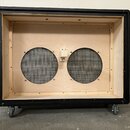 Fotografie znázorňuje otevřený dřevěný box s černým potahem vnějšího rámu. Uvnitř jsou dvě kulaté otvory zakryté kovovou síťkou a uprostřed mezi nimi…