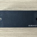 Černý obdélníkový snímač s matným povrchem. V pravém dolním rohu je bílý nápis EMG-HZ. Na levé straně je vidět otvor pro šroub a na pravé straně výře…