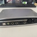 Stříbrné audio rozhraní s černým zadním panelem. Na panelu jsou nápisy „outputs“, „stereo line“, „2/R“, „1/L“ a „inputs“, „stereo mic“, „ch2 inst/lin…