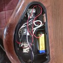 Fotografie zachycuje otevřený prostor pro elektroniku v dřevěném těle nástroje. Uvnitř jsou vidět různobarevné vodiče, zapájené spoje a baterie značk…