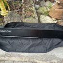 Černý rozkládací stojan v černé přepravní tašce. Na horní hraně stojanu je bílý nápis ULTIMATE SUPPORTS. Povrch stojanu vykazuje drobné škrábance a n…