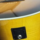 Detail bokové strany akustické kytary s žlutým přechodem do tmavší barvy (sunburst) a bílým lemováním. Na boku je umístěna černá plastová zásuvka s k…