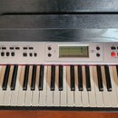 Detailní pohled na ovládací panel a klávesnice elektronického klavíru. Na stříbrném panelu jsou umístěna tlačítka, displej a nápisy jako MASTER VOLUM…