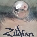 Kruhové činely z kovového materiálu s viditelným broušením povrchu. Na ploše je černý nápis Zildjian®. V horní části u středového bodu je viditelná b…