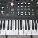 Černý synthesizér s bílými a černými klávesami. V levém horním rohu je logo ASM ASHLEY VOLUME MACHINES a nápis HYDRASYNTH. Panel obsahuje množství ov…