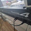 Černý digitální klavír s nápisem TYROS 4. Na zadní straně jsou viditelné konektory a nápisy TO SUB WOOFER, AC IN a TO LEFT SPEAKER. Do přístrojů jsou…