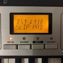 Detailní pohled na ovládací panel klávesového nástroje s displejem a tlačítky. Na oranžovém displeji je text B51 J 138 a pod ním SLIP PAD. Pod disple…