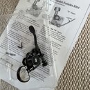 Fotografie zachycuje jeden černý ladicí kolík s mechanismem Hipshot Extender. Na součástí je viditelné logo „HipShot“. Vedle nástroje jsou položeny p…