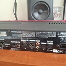 Zadní strana černého elektronického zařízení s červeným horním okrajem. Na zadním panelu jsou různé konektory, včetně MIDI, USB a S/PDIF, s popisky j…