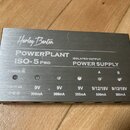Stříbrný napájecí zdroj s kovovým povrchem. Na horní straně je nápis Harley Benton, POWERPLANT ISO-5 PRO a ISOLATED OUTPUT POWER SUPPLY. Zařízení má…