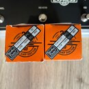 Dvě oranžové krabičky s nápisy Tube Amp Doctor™ a AMP DOCTOR. Na každé krabičce je nalepěná černá štítky s bílým textem: 1993, 6L6GC-STR, 19AM TC:, P…