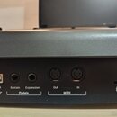 Detail zadní strany černého hudebního nástroje s připojovacími konektory. Jsou zde viditelné nápisy USB, Sustain, Expression, Pedals, Out, MIDI a In.…