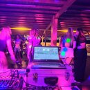 Fotografie zachycuje DJské vybavení v provozu na akci. Na bílém transportním kufru stojí otevřený notebook značky hp, pod ním je umístěn DJ kontrolér…