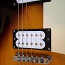 Detail elektrické kytary s tělem v barevném přechodu od žluté po černou. Nástroj má dva bílé humbuckery v černých rámečcích, krémový pickguard a chro…