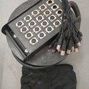Černý kulatý rozvodový box s madlem, který obsahuje 16 ženských XLR konektorů. Konektory jsou očíslovány od 1 do 16 a vedle některých jsou vidět písm…