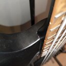 Detailní záběr na spoj hned krku a těla černé kytary. Na hraně těla je viditelný odřap a mírné opotřebení laku. V pravé části jsou vidět hnedkové hma…