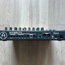 Zadní strana šedého analogového syntetizátoru s nápisem MINIBRUTE ANALOG SYNTHESIZER a logem Arturia. Jsou zde viditelné konektory s popisky CV GATE…