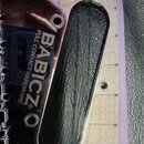 Detail chromovaného kovového dílu s oválným výřezem. Na povrchu je vidět nápis BABICZ® a FULL CONTACT HARDWARE. Povrch vykazuje drobné škrábance a ot…