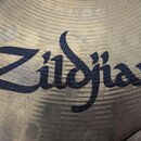 Detailní záběr na povrch mosazného činely s viditelným broušením v koncentrických kruzích. Uprostřed je černý nápis Zildjian. Povrch vykazuje drobné…