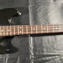 Černá elektrická basová kytara s hnědým hmatníkem a světlou hlavou. Na hlavě je vidět logo Fender a nápis MUSICMASTER Bass. Tělo má černý povrch s vi…