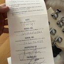 Fotografie zachycuje kontrolní seznam Pre-Pack Checklist položený na kytaru. Na papíře je ručně zapsané datum (3/27/13), model no. LTAAAUGHI a serial…