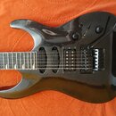 Černá elektrická kytara s lesklým povrchem a metalickými vločkami. Nástroj má jeden humbucker v pozici mostu, jednojedly snímač v pozici krku a Tremo…