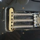 Fotografie zachycuje zadní část kytary s vyřezem v černém lakovaném těle, ve kterém je vidět mechanismus tremola. Jsou zde tři kovové pružiny připoje…