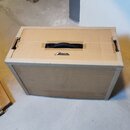 Hnědý přepravní kufr z dřevoplátě s černou plastovou rukojetí. Na horní straně je umístěno logo a nápis FRACTAL AUDIO SYSTEMS. Povrch vykazuje drobné…