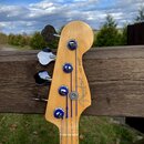 Fotografie zachycuje hlavu basové kytary z přírodního světlého dřeva. Na povrchu je vidět logo Fender, nápis JAZZ BASS® a drobný text MADE IN USA. Me…