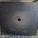 Zadní strana černého kytarového komba potaženého texturovaným vinylen. Uprostřed se nachází kulatý otvor pro ventilaci nebo připojení s kovovým prste…